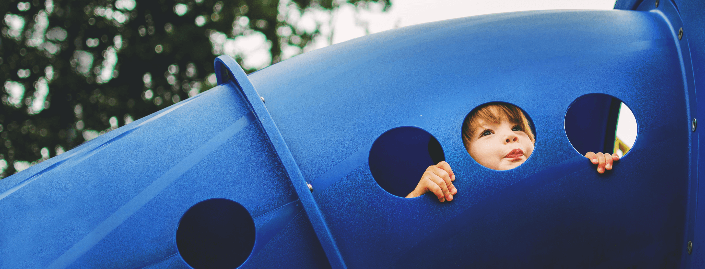 Young child peeking through one of three holes in blue playground equipment.